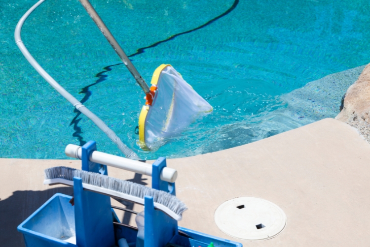 Pool cleaning net and tools near clear blue water.